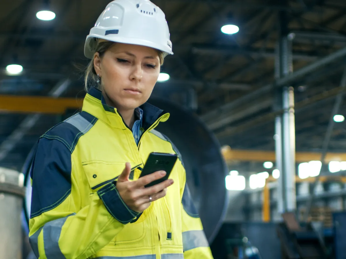 Ingeniera con casco de seguridad usando su teléfono en una planta industrial